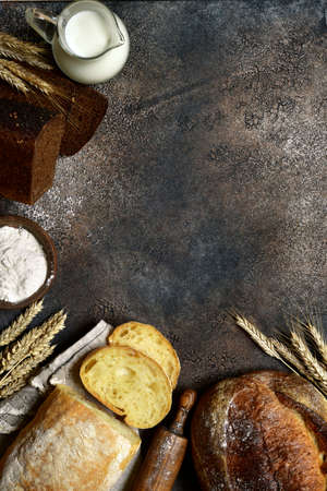 Homemade fresh baked bread with milk, flour and ears on a dark slate, stone or concrete background.の写真素材
