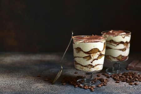 Tiramisu - traditional italian dessert from mascarpone, biscuit and coffee in a glasses on a dark brown slate, stone or concrete background.の写真素材