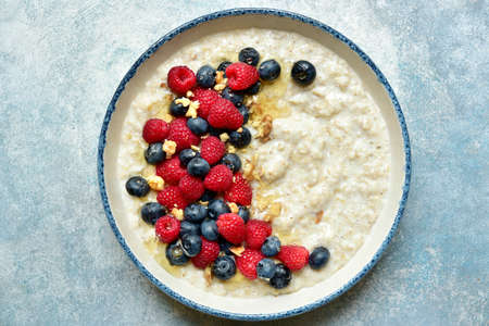 Oatmeal porridge with fresh berries and honey for a breakfast in a bowl over light blue slate, stone or concrete background, Top view with copy space.の写真素材