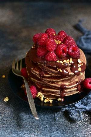 Delicious chocolate pancakes with fresh raspberries on a plate on a dark slate, stone or concrete...