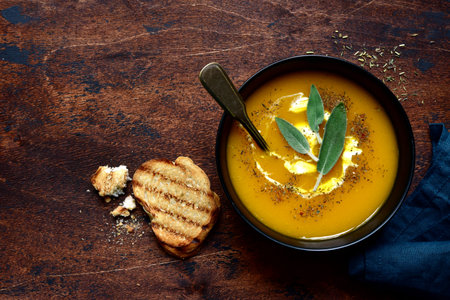 Delicious pumpkin soup with vegan cream and sage in a black bowl on a dark wooden background. Top view with copy space.の写真素材