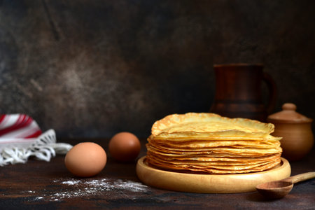 Stack of thin pancakes or crepes on a dark rustic wooden background.