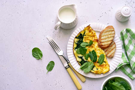 Omelet stuffed with spinach and cheese on a white plate on a light slate, stone or concrete...