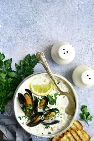 Chowder - delicious fish soup with mussels in a bowl on light gray slate, stone or concrete...