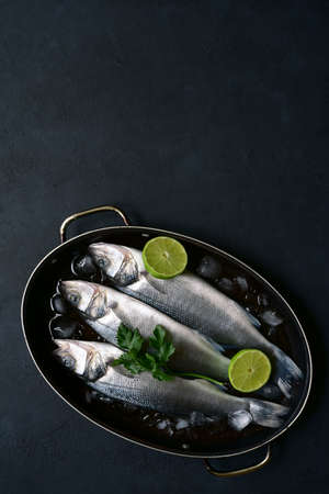 Raw sea bass - organic delicious ocean fish in a skillet pan on dark slate, stone or concrete background. Top view with copy space.の写真素材