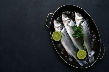 Raw sea bass - organic delicious ocean fish in a skillet pan on dark slate, stone or concrete background. Top view with copy space.の写真素材