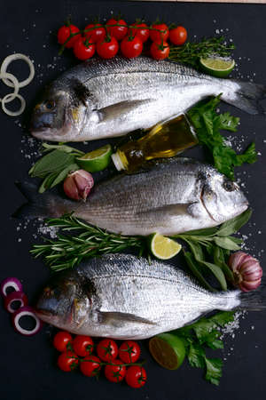 Raw dorado fish or sea bream with ingredients for making on a black slate, stone or concrete background. Top view with copy space.の写真素材