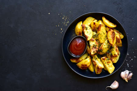 Roasted potato slices with spices with ketchup on a black plate over dark slate, stone or concrete background. Top view with copy space.の写真素材