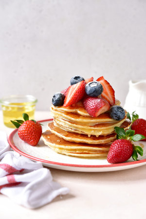 Hot homemade delicious pancake with fresh strawberry and honey on a white plate on a light slate,...