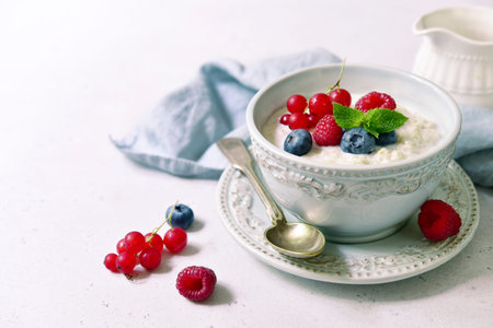Oatmeal porridge with fresh berries and maple syrup for a breakfast in a blue bowl with spoon on a...