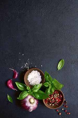 Culinary background with traditional italian spices: basil, garlic, sea salt, pepper and olive oil on a dark slate, stone or concrete table. Top view with copy space.の写真素材