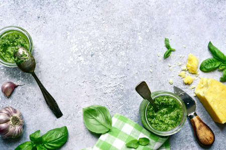 Traditional italian pesto - sauce from basil, cheese, garlic, nuts and olive oil in a jar on a light gray slate, stone or concrete background. Top view with copy space.の写真素材