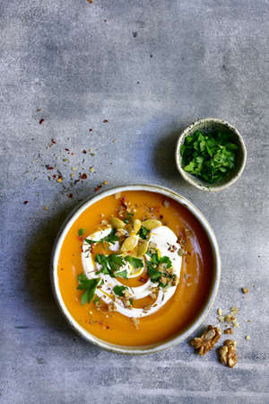 Delicious autumn pumpkin soup with cream and walnuts in a bowl over light gray slate, stone or concrete background. Top view with copy space.の写真素材