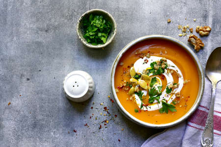 Delicious autumn pumpkin soup with cream and walnuts in a bowl over light gray slate, stone or concrete background. Top view with copy space.の写真素材