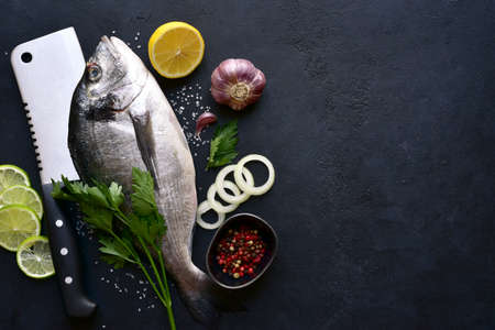 Raw dorado fish with ingredients for making: lemon, herbs, garlic, olive oil and salt on a dark slate, stone or concrete background. Top view with copy space.の写真素材