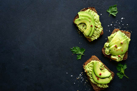 Delicious toasts with guacamole and avocado sliceses on a dark slate, stone or concrete background....