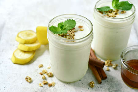 Fresh apple banana smoothie with oatmeal, cinnamon and honey in a mason jars on white slate, stone or concrete background.の写真素材