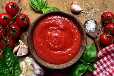 Homemade tomato sauce with ingredients for making in a wooden bowl over rustic background. Top view with copy space.の写真素材