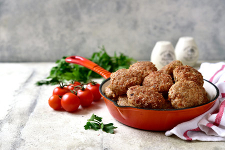 Homemade meat cutlets in a skillet pan on a light slate, stone or concrete background.