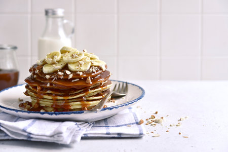 Hot banana pancakes with caramel sauce and nuts on a white slate, stone or concrete background.の写真素材