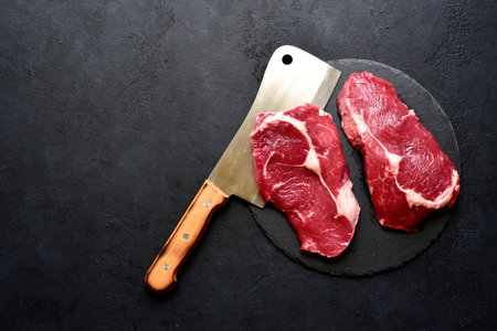 Raw organic rib eye steak with ingredients for making on a dark slate, stone or concrete background. Top view with copy space.の写真素材