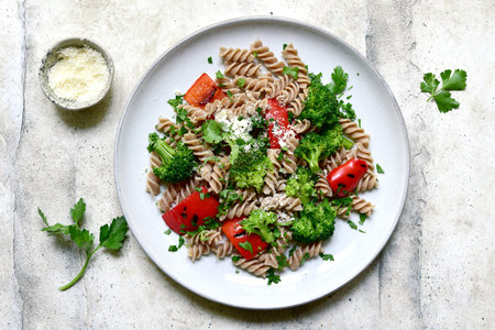 Whole grain pasta fusilli with grilled bell pepper and broccoli on a light gray slate, stone or...