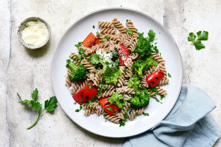 Whole grain pasta fusilli with grilled bell pepper and broccoli on a light gray slate, stone or concrete background. Top view with copy space.の写真素材