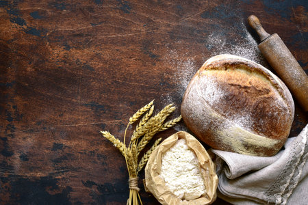 Homemade fresh baked bread with flour and ears on a dark wooden background.の写真素材