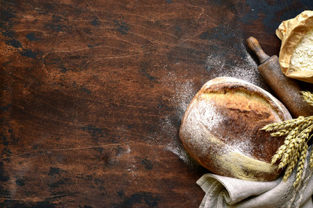 Homemade fresh baked bread with flour and ears on a dark wooden background.