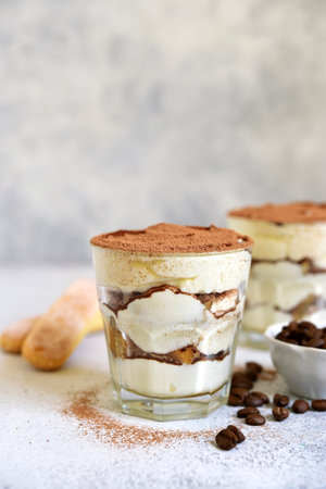 Tiramisu - traditional italian coffee dessert from mascarpone cheese and biscuit in a glass cup on a white slate, srone or concrete background.の写真素材