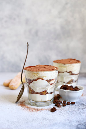 Tiramisu - traditional italian coffee dessert from mascarpone cheese and biscuit in a glass cup on a white slate, srone or concrete background.の写真素材