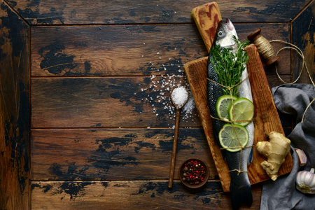 Fresh raw organic sea bass with ingredients for making on a rustic wooden background. Top view with copy space.の写真素材