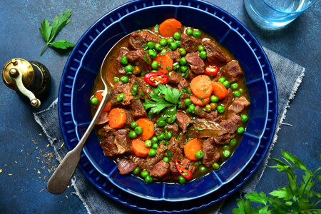 Meat stew with carrot and green pear ( goulash) in a blue bowl over dark slate, stone or concrete background. Top view with copy space.の写真素材