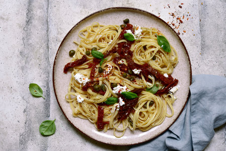 Pasta bavette with dried tomatoes, capers and ricotta on a black plate over light gray slate,stone or concrete background. Top view with copy space.の写真素材