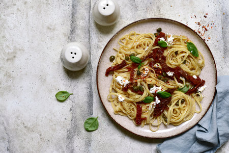 Pasta bavette with dried tomatoes, capers and ricotta on a black plate over light gray slate,stone or concrete background. Top view with copy space.の写真素材