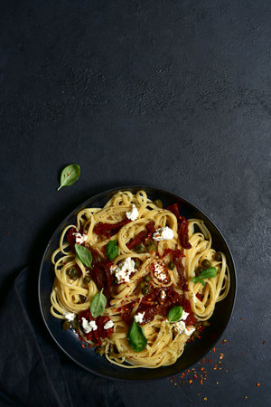 Pasta bavette with dried tomatoes, capers and ricotta on a black plate over dark slate, stone or concrete background. Top view with copy space.の写真素材