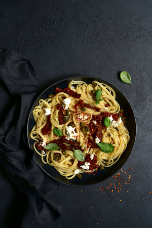 Pasta bavette with dried tomatoes, capers and ricotta on a black plate over dark slate, stone or concrete background. Top view with copy space.の写真素材