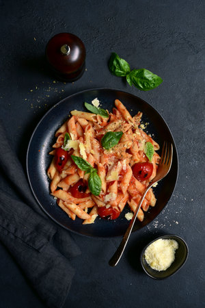 Penne pasta with grilled tomatoes in a black bowl over dark slate, stone or concrete background. Top view with copy space.の写真素材