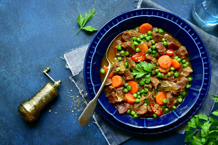 Meat stew with carrot and green pear ( goulash) in a blue bowl over dark slate, stone or concrete background. Top view with copy space.の写真素材
