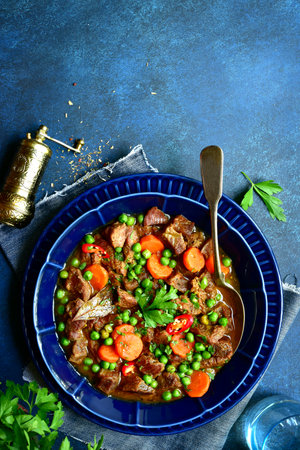 Meat stew with carrot and green pear ( goulash) in a blue bowl over dark slate, stone or concrete background. Top view with copy space.の写真素材