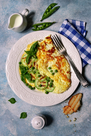 Delicious omelet with green vegetables ( sweet peas and zucchini ) for a breakfast on a white plate over light blue slate, stone or concrete background. Top view with copy space.の写真素材