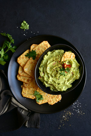 Guacamole - traditional mexican spicy avocado dip in a black bowl on a dark slate, stone or concrete background. Top view with copy space.の写真素材