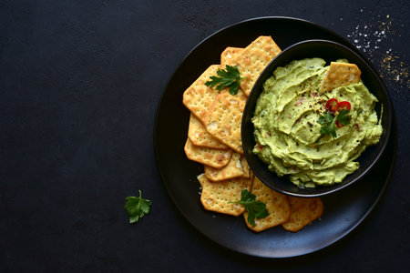 Guacamole - traditional mexican spicy avocado dip in a black bowl on a dark slate, stone or concrete background. Top view with copy space.の写真素材