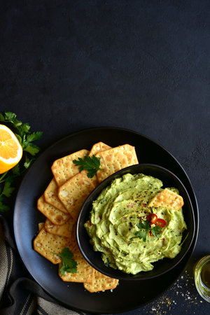Guacamole - traditional mexican spicy avocado dip in a black bowl on a dark slate, stone or concrete background. Top view with copy space.の写真素材