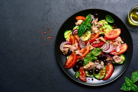 Tuna salad with cucumber and tomato on a black plate over dark slate, stone or concrete background. Top view with copy space.の写真素材