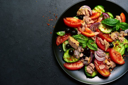 Tuna salad with cucumber and tomato on a black plate over dark slate, stone or concrete background. Top view with copy space.の写真素材