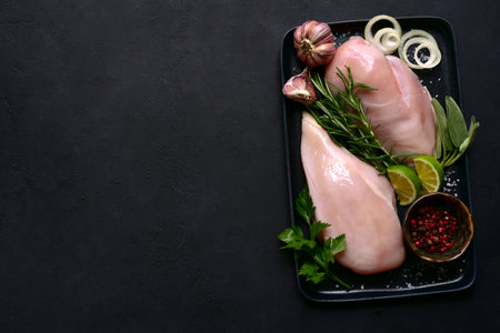 Fresh organic chicken fillet with spices on a black plate over dark slate, stone or concrete background. Top view with copy space.の写真素材