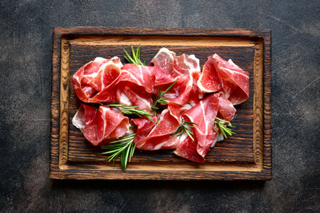 Slices of prosciutto di parma or jamon serrano (iberico) on a dark wooden background. Top view with copy space.の写真素材