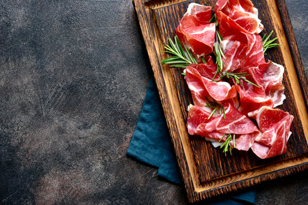 Slices of prosciutto di parma or jamon serrano (iberico) on a dark wooden background. Top view with copy space.の写真素材