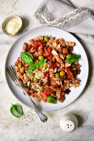 Pasta alla norma, fusilli with eggplants, tomatoes and olives on a plate over light gray slate, stone or concrete background. Traditional dish of Sicilian cuisine. Top view with copy space.の写真素材